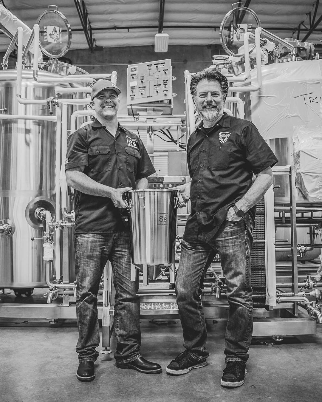 Photo of Ss Brewtech Founders standing in front of an Ss Brewtech Professional Brewhouse while hold a Ss Brewtech Brew Bucket